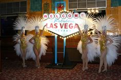 three women dressed in costumes standing next to a sign that reads welcome to fabulous las vegas