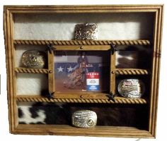 "Our most popular style is now available with a COWHIDE BACK. This Handcrafted Belt Buckle Display Case holds up to 14 Buckles. It will accommodate buckles up to 5\" high. Features handmade molding, Wood rope shelf accents, Black Cast Stars and an 8x10 picture frame for a framed portrait of the buckle winner. Backing is hair on cowhide. Color and style of hide may vary from picture shown. The perfect way to display your buckles from barrel racing, bull riding, or any other rodeo award. Very west Rodeo Awards, Rustic Belt