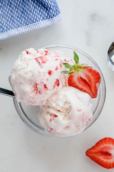 two scoops of ice cream with strawberries on top in a white bowl sitting on a wooden table