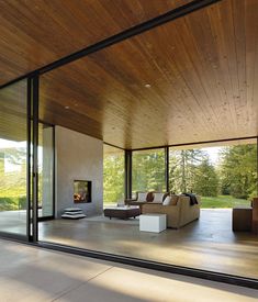 an open living room with glass walls and wood ceilinging on the outside, looking out onto trees