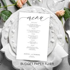 a white plate topped with a menu next to silverware and pink rose flowers on top of it