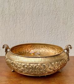 a golden bowl sitting on top of a wooden table with a candle in the middle