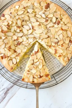 a cake with almonds is on a wire rack and has a slice missing from it