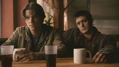 two young men sitting at a table with mugs