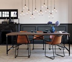 a dining room table with chairs and lights hanging from it's ceiling, in front of a fireplace