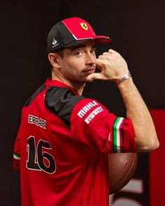 a man in a red shirt and black hat holding a football on his left hand