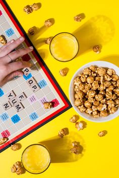 a board game with nuts and drinks next to it on a yellow surface, top view