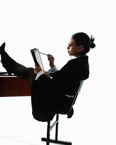 a woman sitting in a chair with her legs crossed and writing on a clipboard