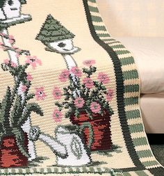 a crocheted blanket with flowers and birds on it sitting on a couch next to a white chair