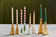 christmas candles are lined up on a table with trees in the middle and one candle is lit