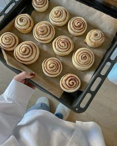 a person holding a pan filled with cinnamon rolls