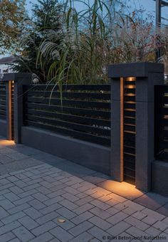 the lights are on in front of the black fence and planters that have plants growing out of them