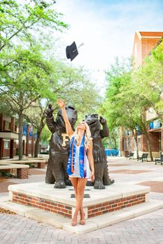 a young woman is throwing her graduation cap in the air while standing next to a bear statue