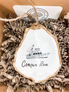 an ornament with a boat on it in a cardboard box that says compass rose