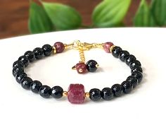 Elevate your style with the protective and vibrant energies of Black Tourmaline and the fiery beauty of African Ruby in this exquisite gemstone bracelet. It features 6mm Black Tourmaline faceted stones known for their grounding and protective qualities. At the heart of this bracelet lies an 8mm Grade A+ African Ruby facetted stone, exuding passion and vitality.  To enhance its elegance, the bracelet is elegantly accented with 24K gold-plated stainless-steel beads that add a touch of luxury to yo Black Tourmaline Bracelet, Black Tourmaline Stone, Meditation Bracelet, Tourmaline Bracelet, Yoga Bracelet, Tourmaline Stone, July Birthstone, Ruby Gemstone, Black Tourmaline