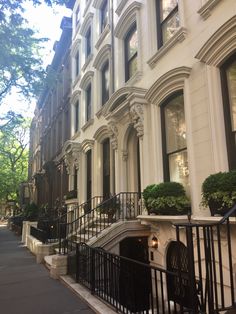 a row of white townhouses with black railings and trees in the front yard