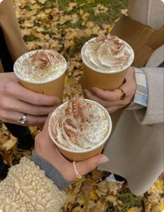 three people holding cups of coffee in their hands with autumn leaves on the ground behind them