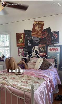 a woman laying on top of a bed in a room with posters above her head