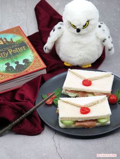 two sandwiches on a plate next to a book and an owl figurine with a knife