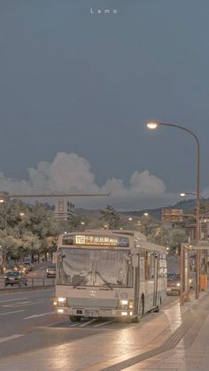 a bus driving down a street next to a traffic light at night with clouds in the sky