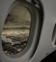 an airplane window with the view of a city at night from it's wing