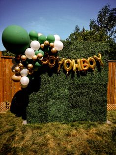 balloons and confetti are hanging from the top of a tall green wall that says happy on it