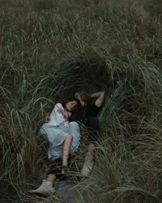 two people are laying in the tall grass, one is hugging the other's head