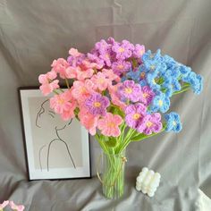 crocheted flowers are in a vase next to a framed photo and small marshmallows