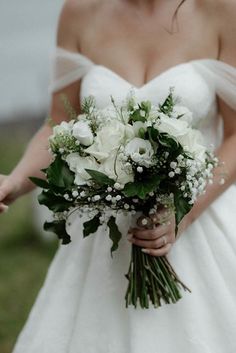 a woman in a white dress holding a bouquet of flowers and greenery on her wedding day