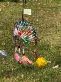 a wind chime with feathers and beads hanging from it's side in the grass