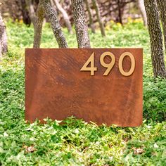 a sign that is in the grass next to some trees and bushes with numbers on it