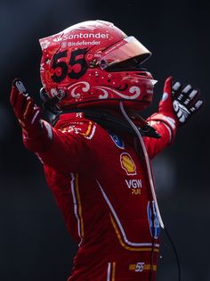 a man wearing a red racing suit and helmet holding his hands up in the air