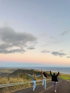 two girls jumping up in the air on a road by the ocean with their arms raised