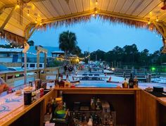 a bar with lots of bottles and glasses on it next to the water at dusk