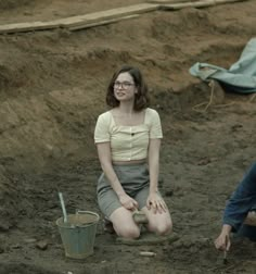 a woman sitting on the ground next to a man with a bucket and shovel in front of her