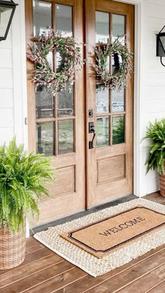 two potted plants sitting on the front porch next to a door with wreaths