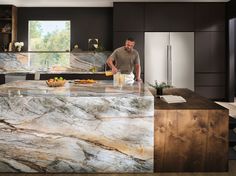 a man standing in a kitchen next to an island with marble counter tops and cabinets