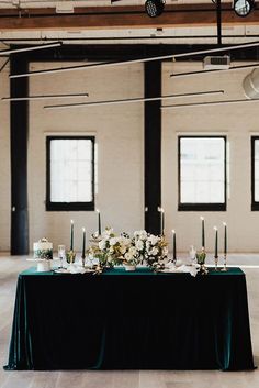 a table with candles and flowers on it in an empty room next to two windows