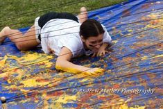 a woman laying on top of a blue tarp covered in yellow and orange paint