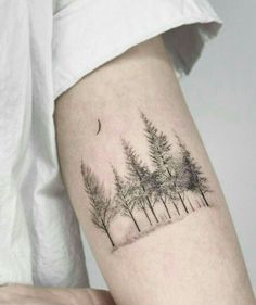 a person with a tattoo on their arm that has trees and a moon in the background