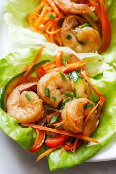 two lettuce wraps with shrimp and carrots on them, sitting on a white plate