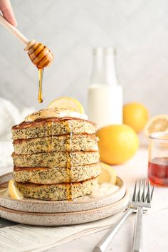 a person drizzling honey onto a stack of pancakes with lemons on the side