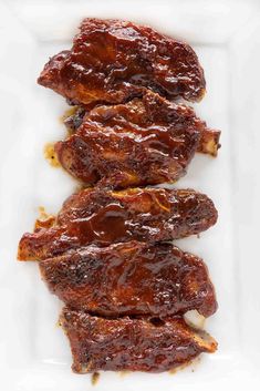 three pieces of barbecue ribs on a white plate with bbq sauce in the middle