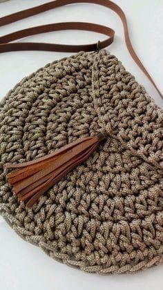 a crocheted purse with a tasseled strap and a brown leather handle