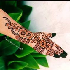 a woman's hand with henna tattoos and flowers on the palm, next to green leaves