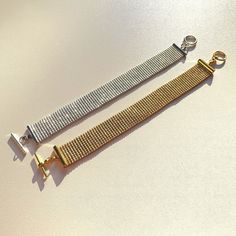 two metal bracelets sitting next to each other on a white surface with gold clasps