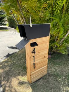 a wooden mailbox sitting in the grass next to some palm trees and bushes with numbers on it