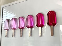 four different colored ice cream pops are lined up on a white surface, and one is pink