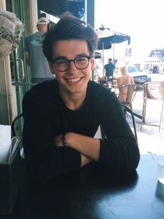 a young man sitting at a table with his arms crossed and looking into the camera