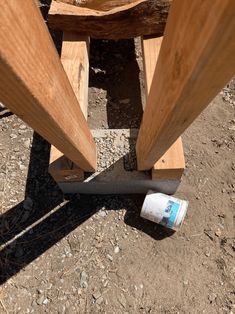 a wooden bench sitting on top of a dirt ground next to a can of paint